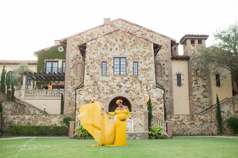 Deidra looking down at her pregnant belly in her yellow maternity gown